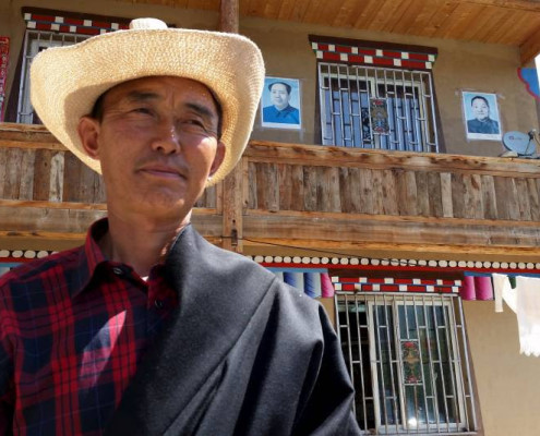 A guest house owner stands in front of his property with posters of late Chinese Communist Party Chairman Mao Zedong and leader Deng Xiaoping on the wall, in Aba Tibetan and Qiang Autonomous Prefecture, Sichuan province, at the end of July. | REUTERS